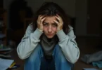 Person overwhelmed by emotions, holding head with hands, illustrating emotional flooding and mental overwhelm.